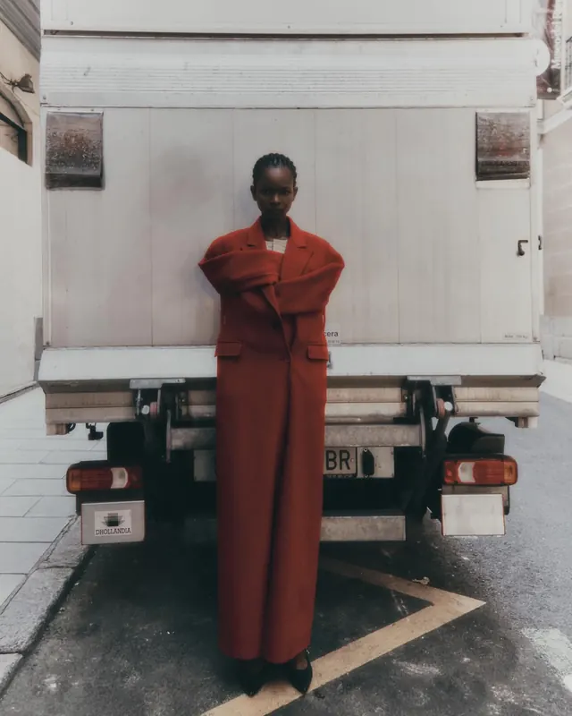 Red oversized coat on truck backdrop, editorial, photographic, vibrant