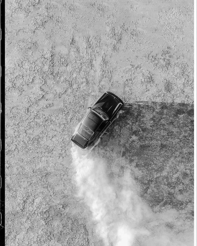 Drifting car on cracked dry lakebed, photographic, minimal, monochrome