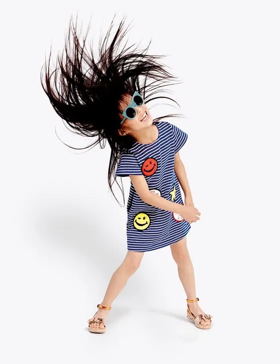 Girl tossing hair in striped patch dress, playful, photographic, light