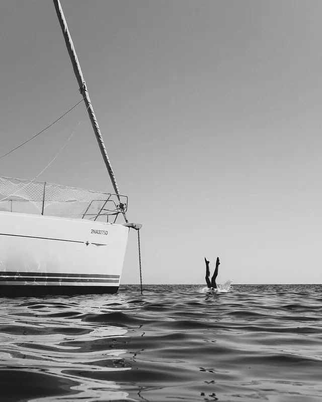 Diver legs beside sailboat, minimal, photographic, monochrome
