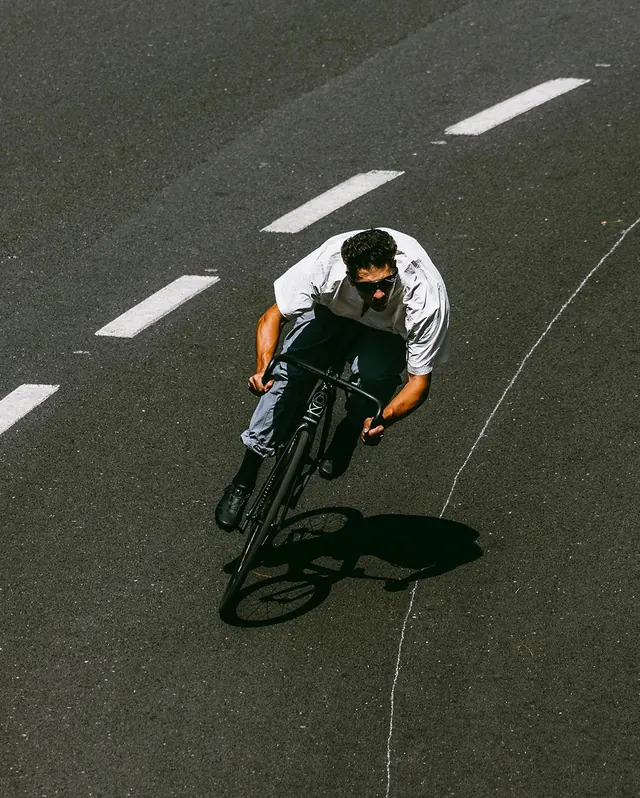Top-down cyclist in white shirt on asphalt, photographic, minimal, dark