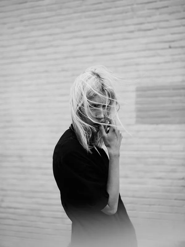Wind-blown hair portrait against brick wall, photographic, minimal, monochrome