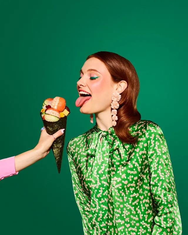 Woman with sushi handroll on green backdrop, photographic, playful, vibrant