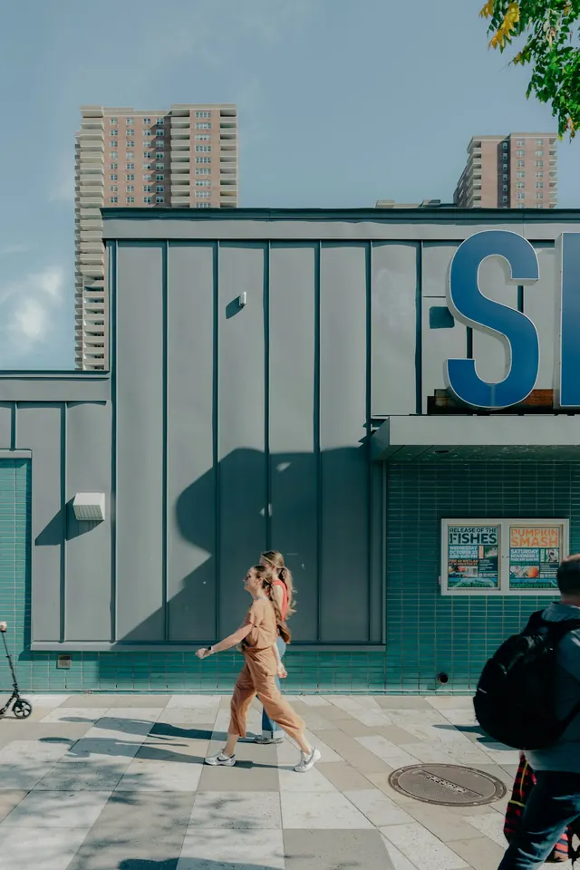 Women walking past modern building with blue signage, photographic, editorial, light