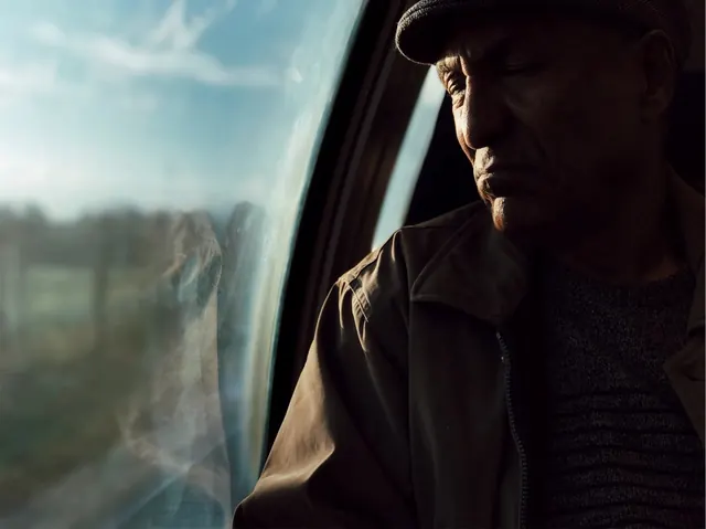 Older man portrait by train window, photographic, editorial, warm