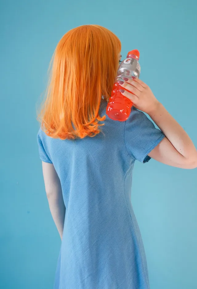 Woman with orange wig holding red toy robot, playful, photographic, vibrant