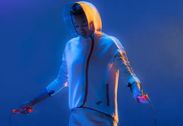 Figure in neon-lit jacket on blue background, photographic, gradient-heavy, vibrant