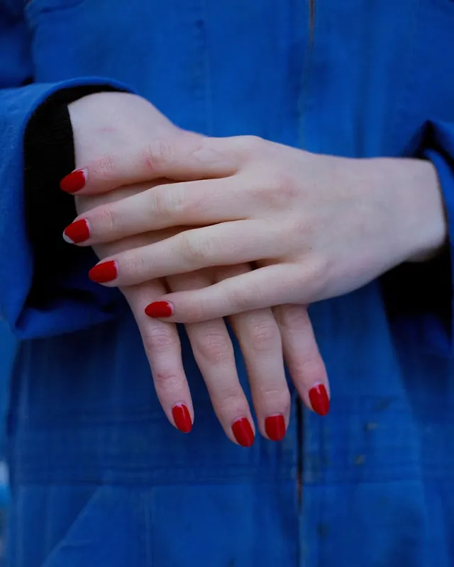Hand with red manicure against blue background, photographic, minimalist, dark