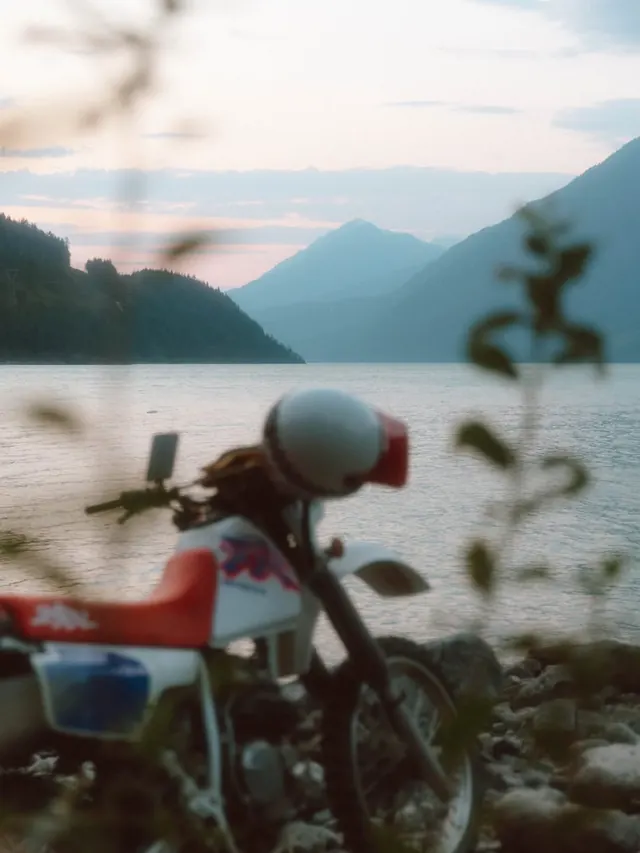 Motorcycle on rocky lakeshore at golden hour, photographic, organic, warm