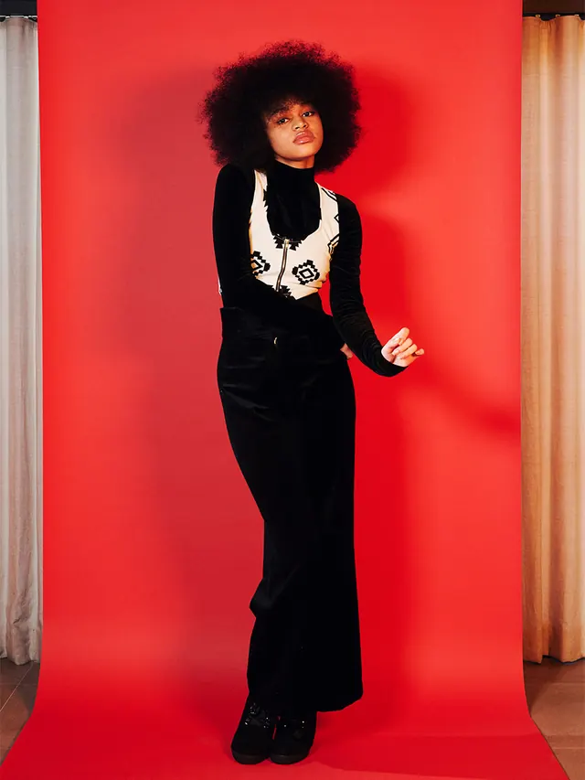 Portrait of figure in black outfit against red background, photographic, bold, vibrant
