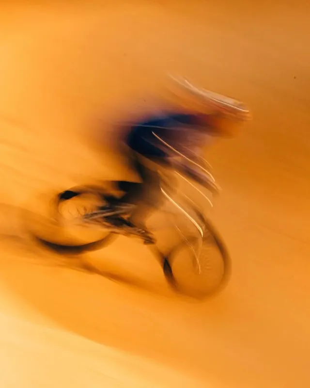Motion-blurred cyclist on orange gradient background, photographic, technical, warm
