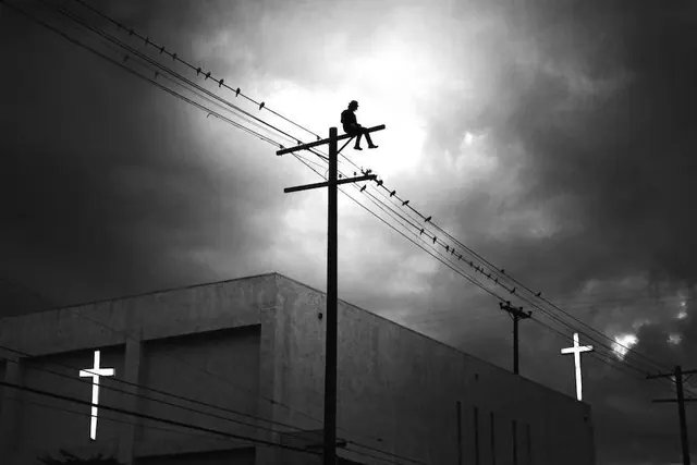 Black and white dramatic landscape photograph with figure on utility pole, photographic, monochrome, dark