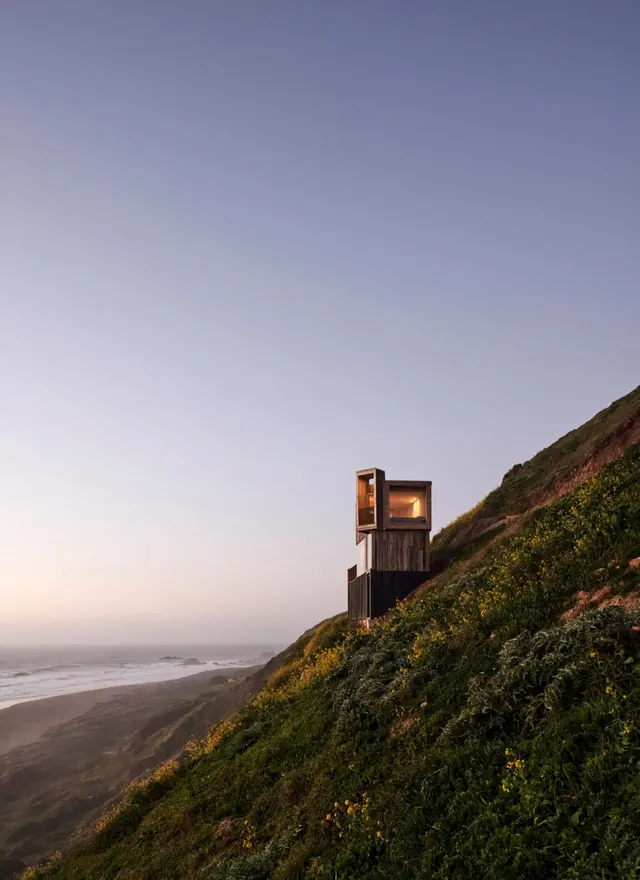Clifftop cabin at dusk with ocean view, minimal, photographic, cool