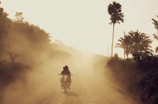 Motorcyclist on dusty tropical road at sunrise, photographic, organic, warm