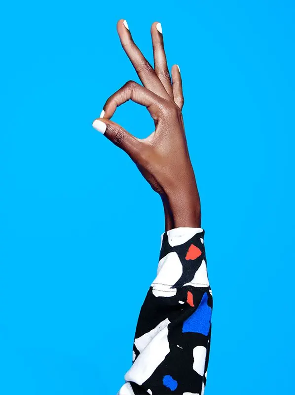 Hand in OK gesture with patterned sleeve against bright blue, photographic, minimalist, vibrant