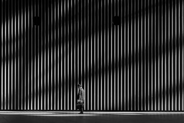 Figure against vertical ribbed wall, brutalist, photographic, monochrome