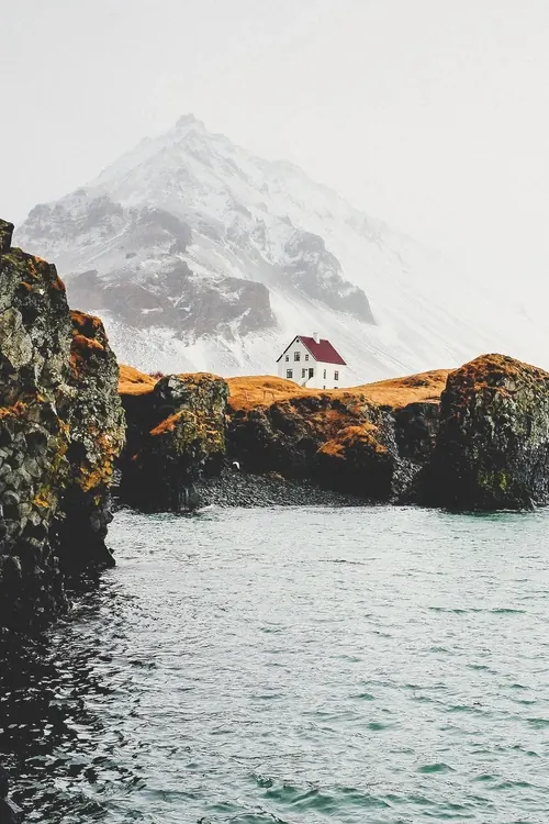 Red roof house by fjord with snow mountain, photographic, minimal, muted