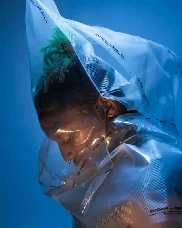Figure wrapped in plastic against blue sky, photographic, conceptual, cool