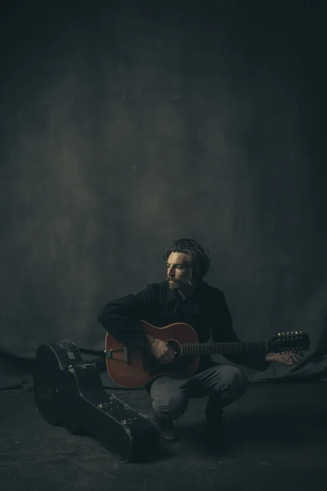 Musician crouching with guitar, photographic, minimal, dark
