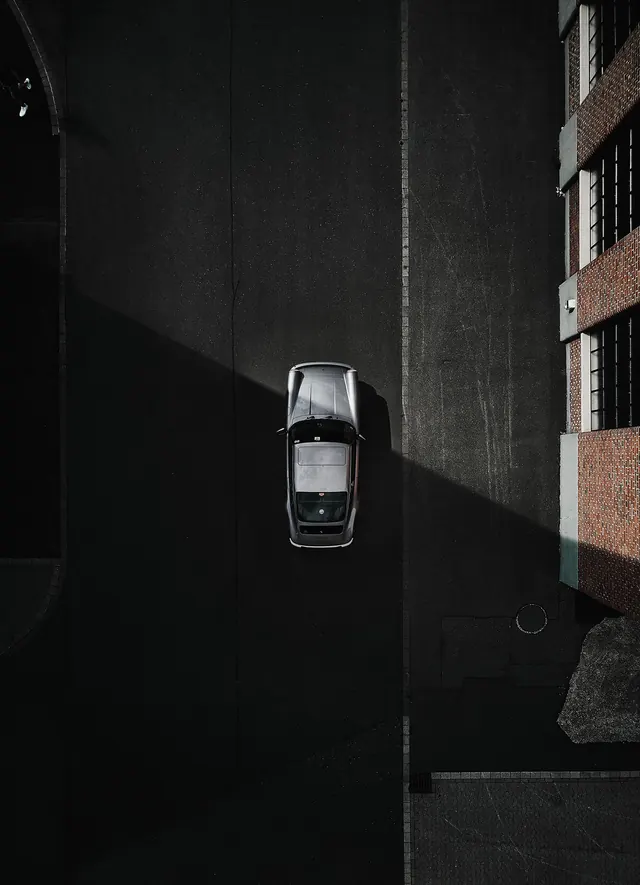 Aerial silver coupe beside brick wall, photographic, minimal, monochrome