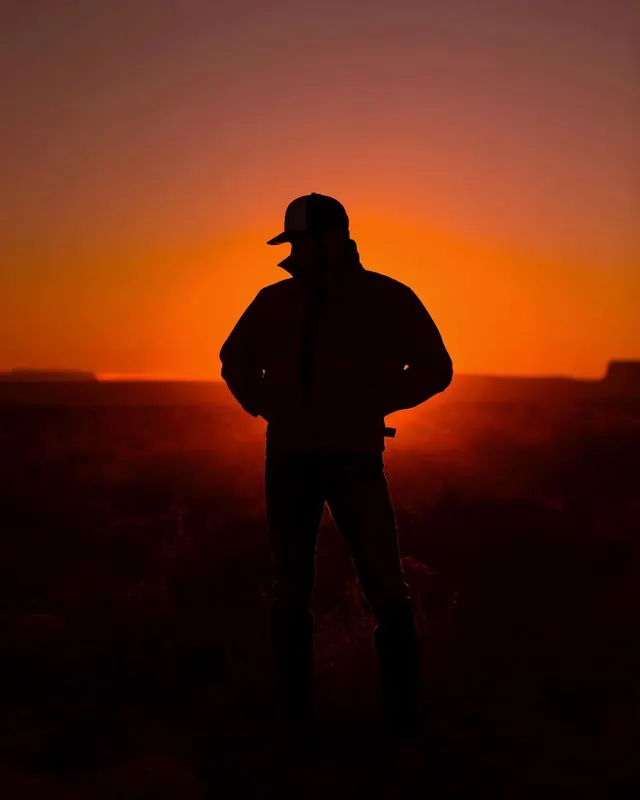 Silhouetted figure in orange desert sunset, photographic, minimal, warm