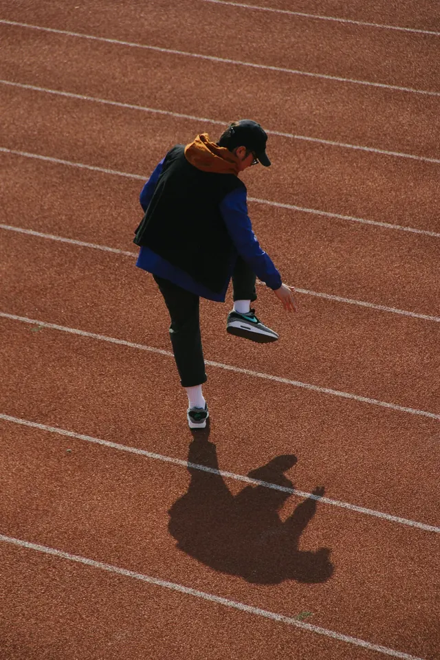 Layered streetwear figure on running track, photographic, minimal, warm