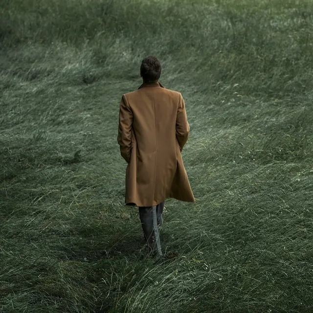 Figure in field wearing ochre coat, photographic, editorial, warm