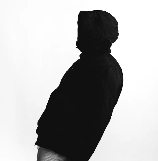 Silhouette figure in dark jacket against light background, minimal, editorial, dark