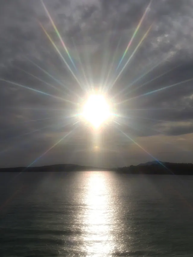 Sunrise over water with dramatic light rays, photographic, dramatic, warm