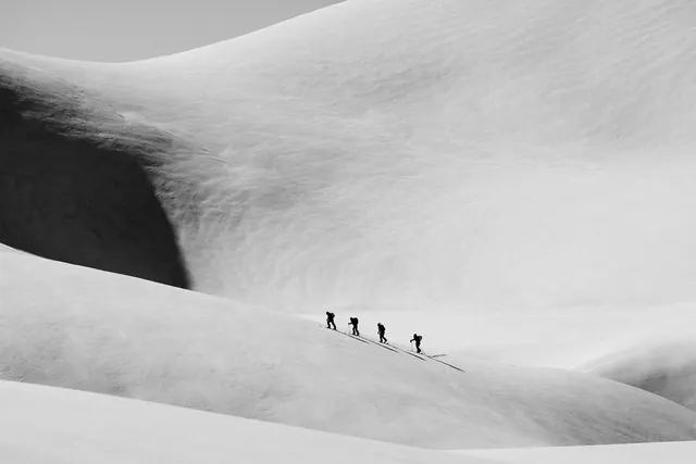 Skiers descending snow-covered mountain slope, photographic, minimal, monochrome