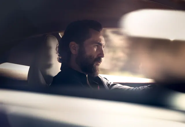 Bearded man in luxury car interior at dusk, photographic, minimal, dark