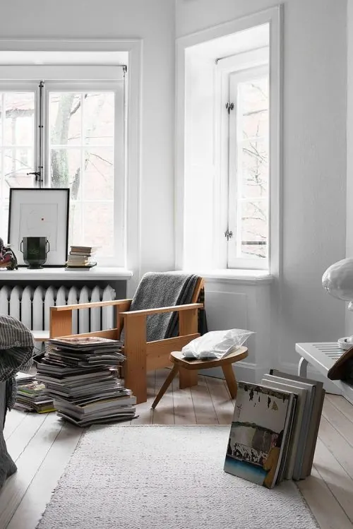 Minimalist white interior with wooden chair and magazine stacks, minimal, photographic, light