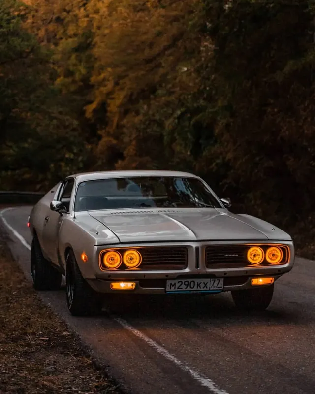Classic silver muscle car with glowing headlights on winding road, photographic, warm