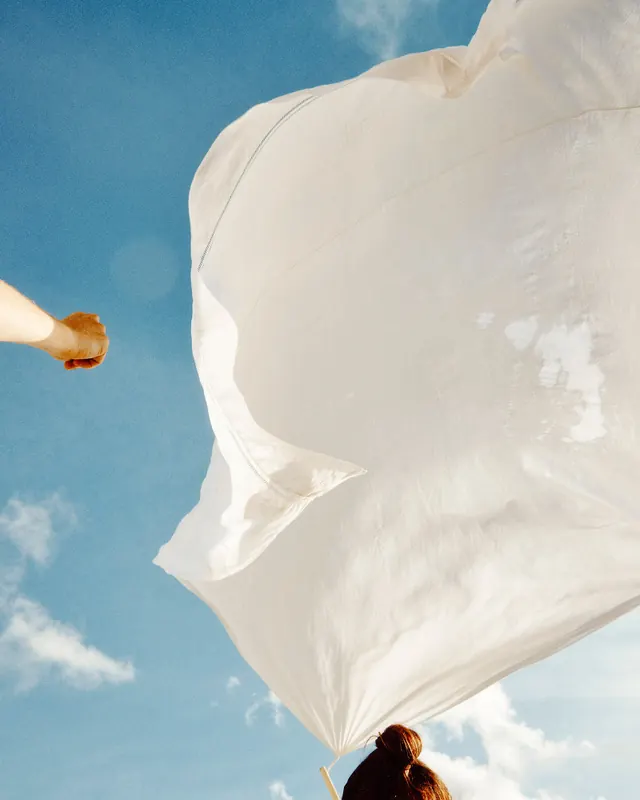 Woman with flowing white fabric against blue sky, photographic, light-mode, light