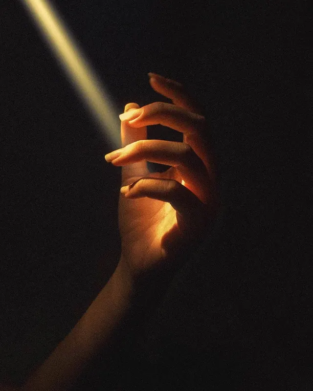 Hand holding stone with warm light, photographic, minimal, dark