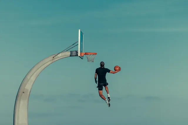 Basketball player mid-air against turquoise sky, minimal, photographic, cool