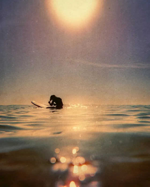 Surfer in ocean at golden hour with atmospheric glow, photographic, organic, warm