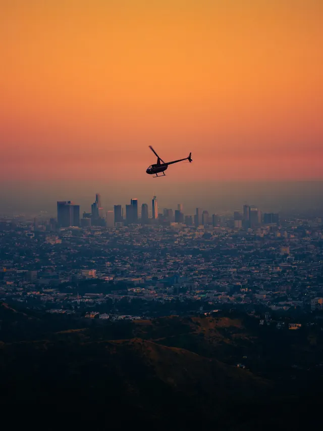 Helicopter against sunset cityscape, photographic, editorial, warm