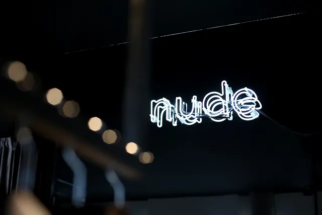 Neon "nude" sign at night with bokeh lights, photographic, dark-mode, dark