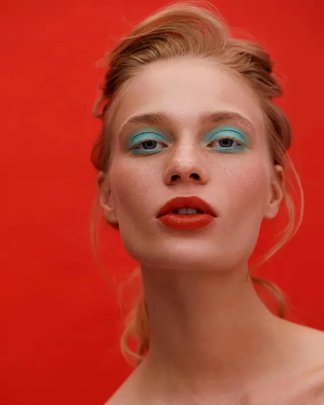 Portrait with turquoise eyeshadow on red background, photographic, editorial, vibrant