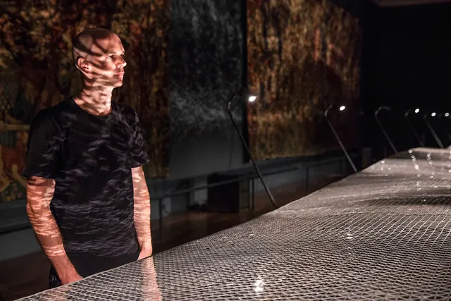 Person in exhibition space with metallic textured installation, technical, dark-mode, dark