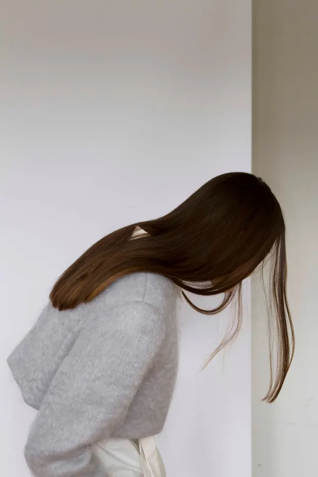 Minimalist figure with long dark hair against neutral wall, minimal, photographic, light