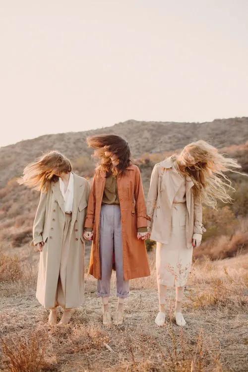 Three people in neutral and rust-toned coats outdoors, photographic, editorial, earthy