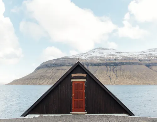 Black boathouse with red door on mountainside, photographic, minimal, high-contrast