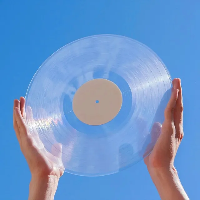Clear vinyl record held against blue sky, photographic, minimal, cool