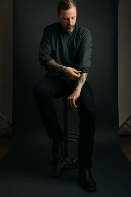 Portrait of man with tattoos in dark setting, photographic, corporate-clean, dark