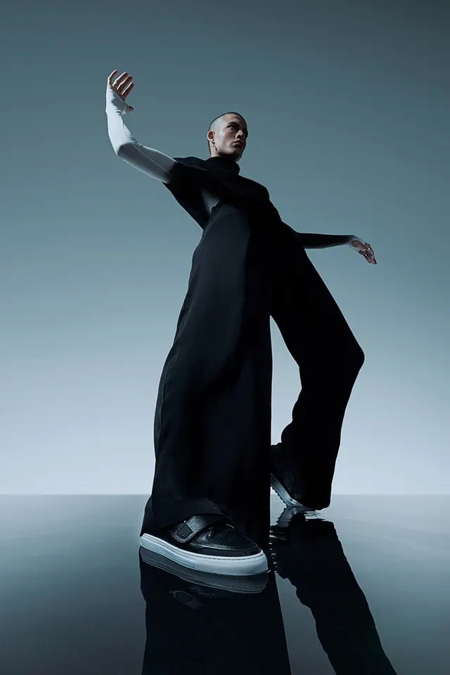 Male model in dark oversized coat and white gloves against blue sky, photographic, editorial, cool