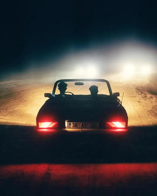 Silhouetted convertible with headlights on desert road at dusk, photographic, dark-mode, dark