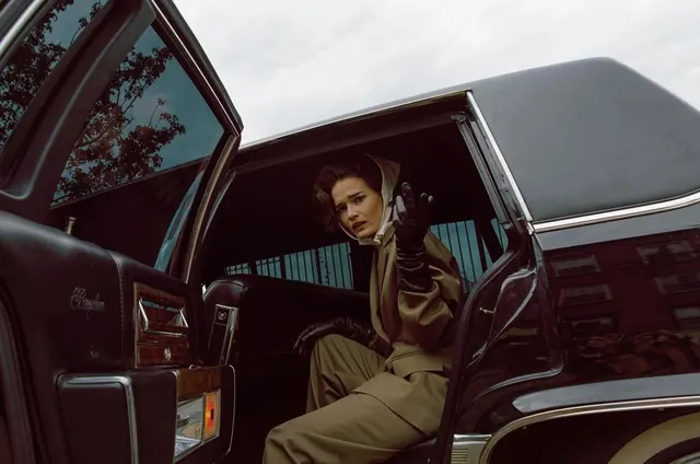 Woman in tan jumpsuit in vintage limousine, editorial, photographic, dark