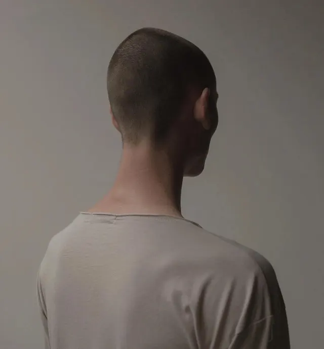 Rear view portrait of person in plain neutral t-shirt against gray background, photographic, minimal, monochrome
